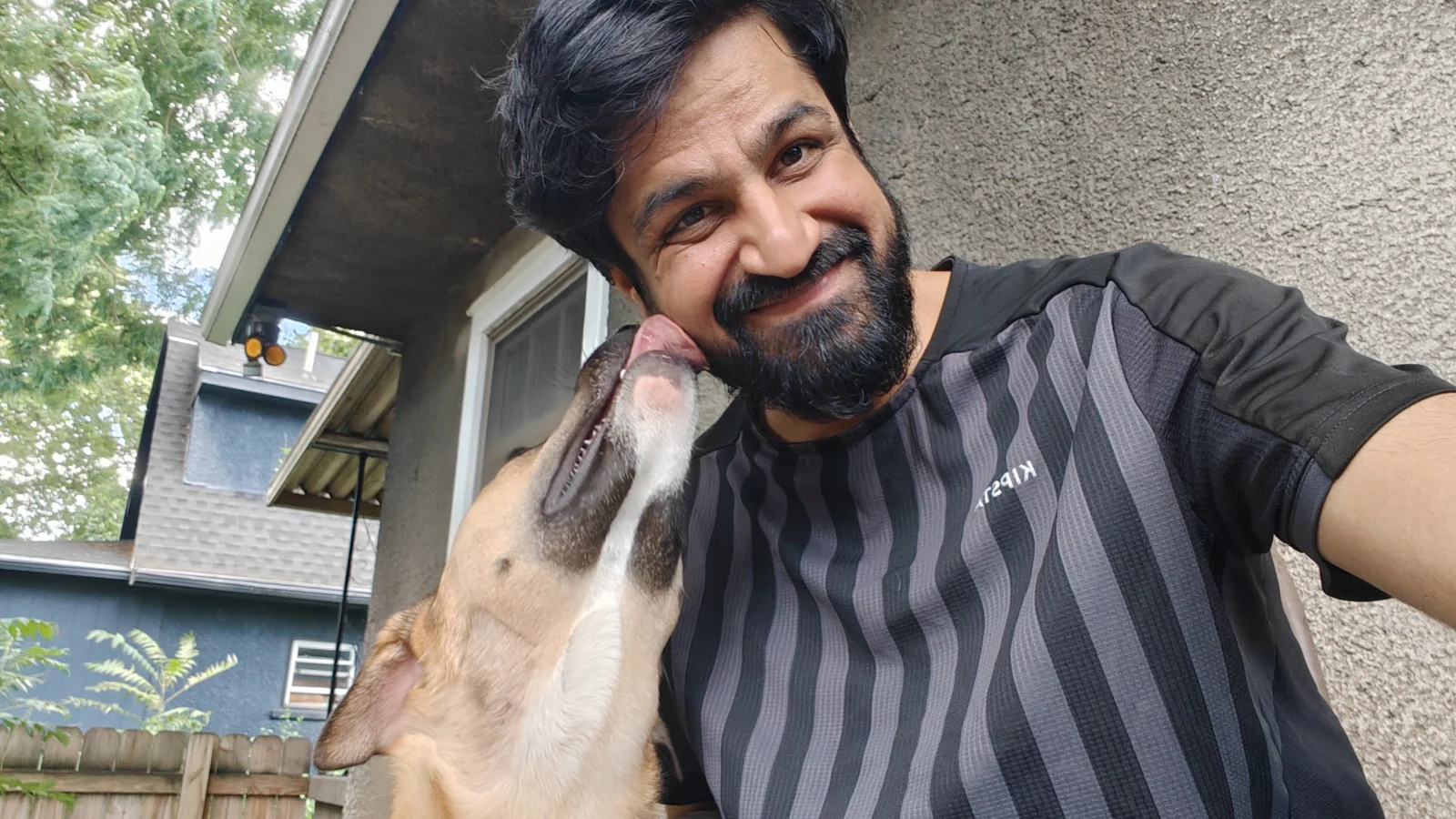 Jay smiling as Joey, a tan-and-white dog, licks his cheek outdoors